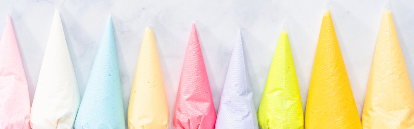 An image of icing bags of various pastel colors, laying flat on a marble surface.