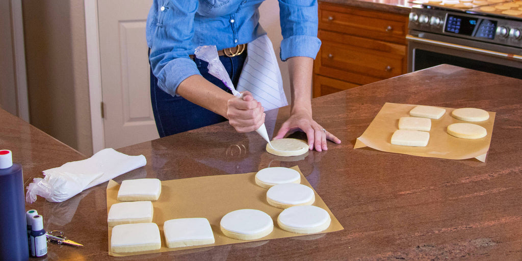 Image of a woman piping icing onto a round cookie in a kitchen.