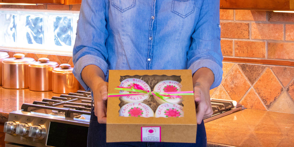 Image of a woman holding a box of 4 cookies.